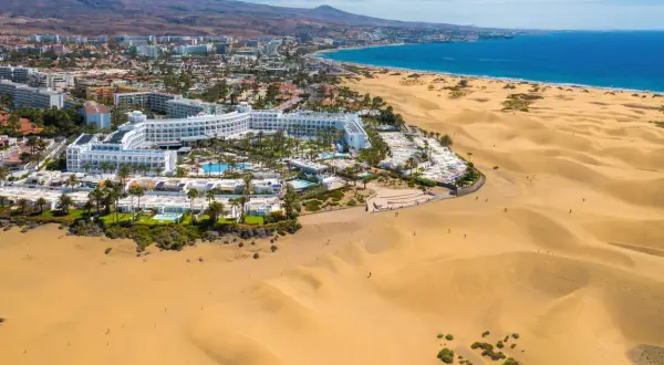 Das Riu Palace Maspalomas thront majestätisch am Rande der goldenen Dünen, mit dem blauen Meer im Hintergrund.