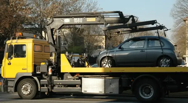 Gelber Abschleppwagen mit grauem Kleinwagen auf der Ladefläche. Ein unerwarteter Stopp, die abschleppkosten 400 euro sind ärgerlich.