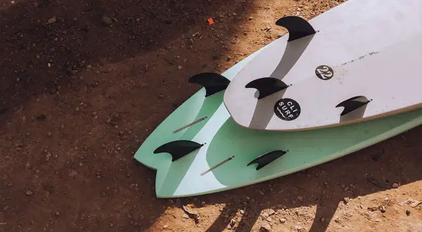 Zwei Surfbretter mit Finnen liegen auf sandigem Boden. Perfekt für die packliste surfcamp.