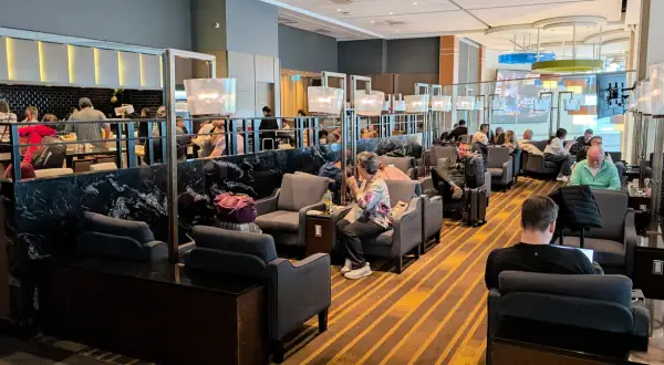 Gemütliche Sitzecken und ein Buffetbereich in einer **priority lounge**. Reisende entspannen sich, arbeiten oder essen.