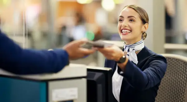 Lächelnde Flugbegleiterin am Schalter reicht einen Pass zurück. Ein Beispiel für Flughafen-Begriffe im Einsatz.
