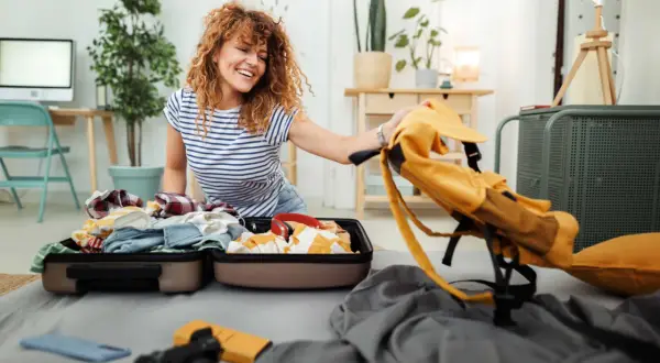 Frau packt Koffer für ihr Auslandssemester. Die Auslandssemester Packliste ist fast komplett, nur noch der gelbe Rucksack fehlt.