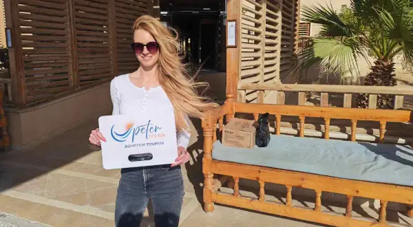 Frau in Hurghada Kleidung, mit Sonnenbrille, hält ein Schild von Peter Tours. Sie trägt Jeans und ein weißes Oberteil.