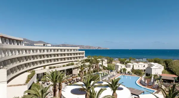 Agapi Beach Resort mit geschwungener Architektur, Pool und Palmen am Meer.