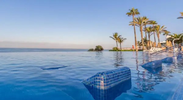 Infinity-Pool mit Blick auf das Meer und Palmen am Riu Palace Meloneras. Entspannung pur im blauen Wasser.