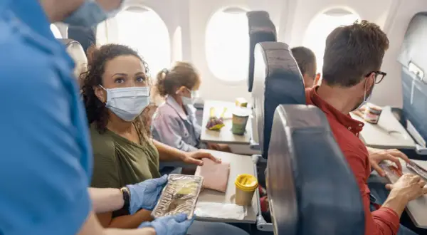 Fliegen mit FFP2-Maske: Eine Frau erhält ihr Essen im Flugzeug. Andere Passagiere tragen ebenfalls Masken.