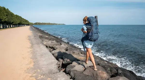 Frau mit großem Rucksack wandert über Felsen am Meer. Perfekte Packliste für Bali!