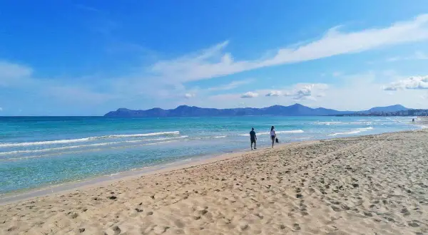 Traumhafter Strand auf Mallorca mit türkisfarbenem Meer und sanften Wellen. Zwei Personen genießen ihren Urlaub.