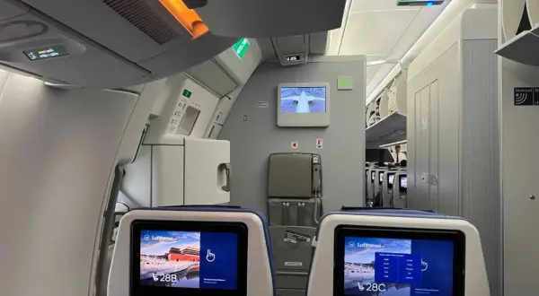 Blick in die Flugzeugkabine. Bildschirme zeigen "Lufthansa" und Sitzplatz 28B/C. Hier erfährst du, wo man im Flugzeug am besten sitzt.