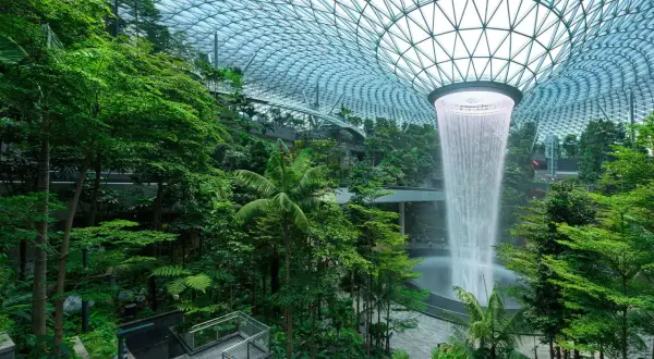 Imposanter Wasserfall im tropischen Garten des Flughafens Singapur. Die beeindruckende Architektur und üppige Vegetation lassen die **Singapur Flughafen Kosten** vergessen.