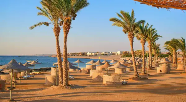 Sonnige Strandkulisse in Hurghada mit Palmen, Sonnenschirmen und Liegen. Perfekt für die Packliste Hurghada!