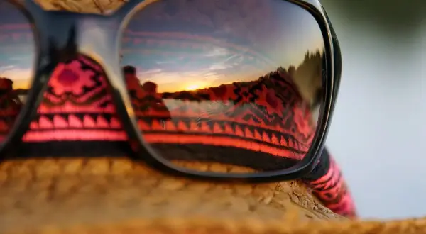 Sonnenuntergangsreflexion in Sonnenbrille auf einem Strohhut. Perfekt für die Packliste Brasilien, mit einem Hauch von Ethno-Muster.