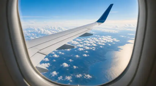 Flugzeugfenster mit Blick auf Flügel, Wolken und Küste. Ein Gabelflug ist eine Reise mit zwei Zielen.