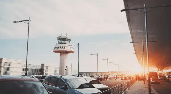 Autos parken am Flughafen Barcelona, mit dem markanten Kontrollturm im Hintergrund.
