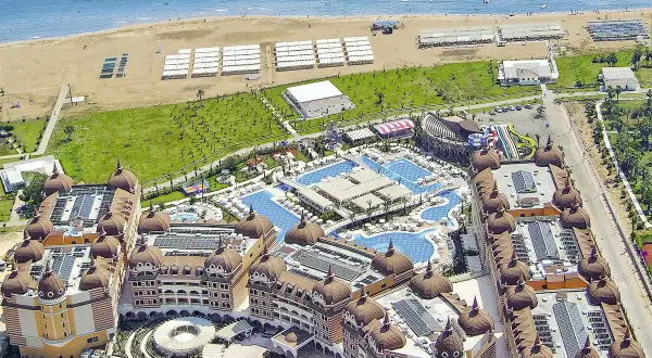 Luftaufnahme eines luxuriösen Resorts mit Kuppeldächern, Pools und Wasserrutschen, das an einen Strand grenzt. Ein Hauch von royal alhambra palace.
