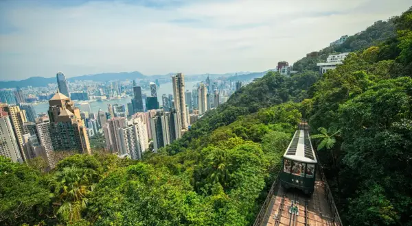 Blick auf die Skyline von Hongkong mit der Peak Tram, die durch üppigen Dschungel fährt. Perfekt für einen Hongkong Urlaub!