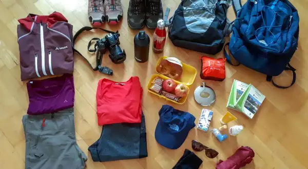 Packliste Wandern Tagestour: Kleidung, Rucksack, Kamera, Verpflegung, Trinkflasche, Wanderstiefel, Sonnenbrille, Regenschirm und Karten für die Tour.