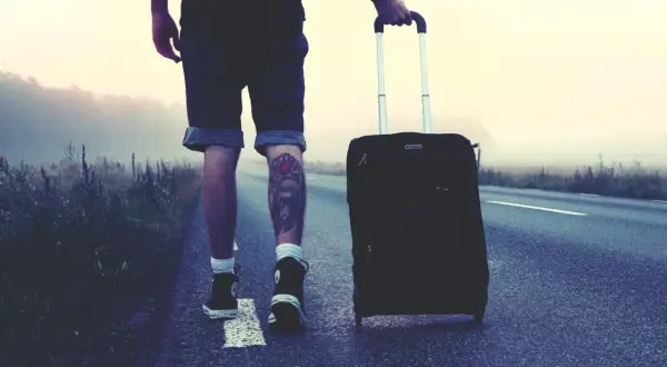 Mann mit Koffer auf einsamer Straße, bereit für London. Die Packliste ist komplett, das Abenteuer beginnt.