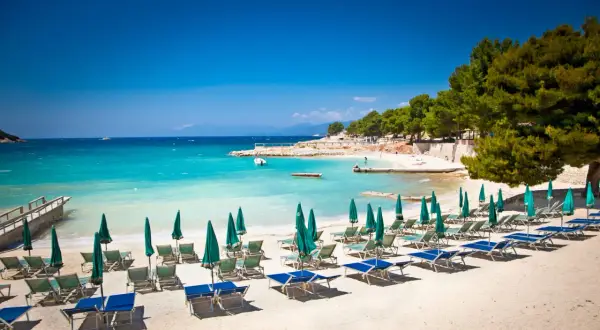 Ein sonniger **Tirana Strand** mit türkisfarbenem Wasser, Liegestühlen und Sonnenschirmen.