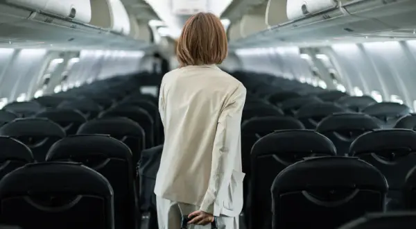 Frau mit Koffer im Gang eines leeren Flugzeugs, bereit für ihren Flug. Sie hat den **priority flughafen** Service gebucht.