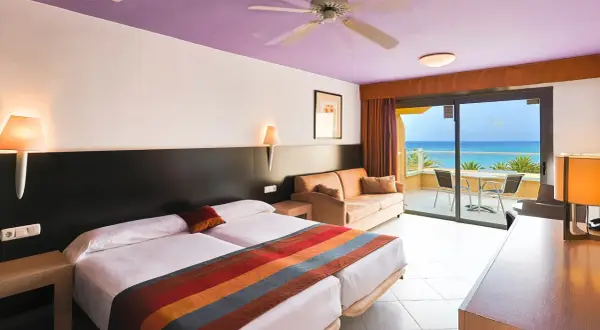 Gemütliches Zimmer im SBH Monica Beach Resort mit Meerblick. Zwei Betten, Sofa und Balkon laden zum Entspannen ein.