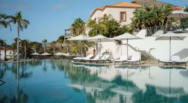 Traumhafter Poolbereich mit Liegen und Sonnenschirmen im Dreams Madeira Spa & Marina. Palmen und ein elegantes Gebäude im Hintergrund.