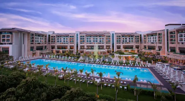 Ein luxuriöses Resort mit einem riesigen Pool und Palmen, das an das **Regnum Carya** erinnert. Abenddämmerung mit rosa Himmel.