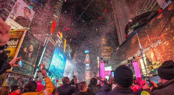 Konfetti regnet auf die Menge am Times Square. Ein Feuerwerk erhellt den Himmel, während die Menschen den Jahreswechsel feiern. Silvester in New York ist ein unvergessliches Erlebnis.