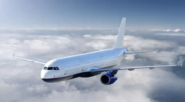 Ein weißes Flugzeug fliegt über einer Wolkendecke. Die Sonne scheint, aber die Wolken deuten auf mögliche Flugzeugturbulenzen hin.