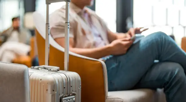 Mann mit Koffer im Wartebereich, bereit für die Dienstreise. Die Packliste für die Dienstreise ist vollständig.