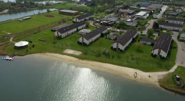 Luftaufnahme des Wangerland Resorts mit Gebäudekomplexen, einem See und einem Strand.