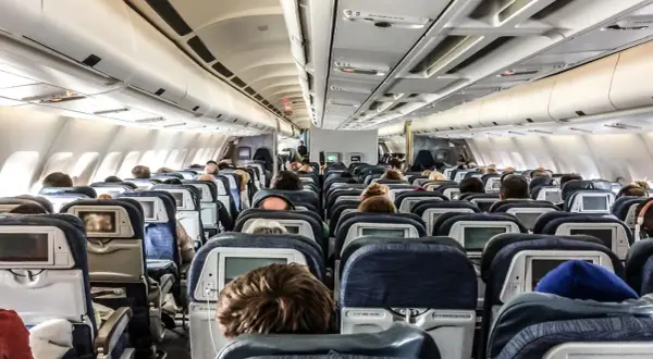 Blick in die Kabine eines Flugzeugs mit vielen Reihen von Langstreckenflug Sitzen, einige mit Bildschirmen.