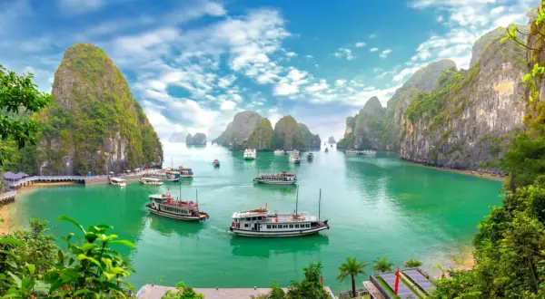 Traumhafte asien reiseziele: Boote gleiten durch smaragdgrünes Wasser, umgeben von steilen, bewachsenen Karstfelsen im Halong-Bucht.