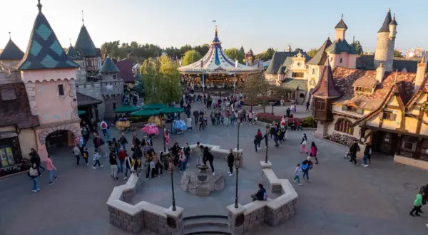 Bunte Märchenhäuser und ein Karussell beleben den Platz. Eine lebhafte Menge schlendert umher, perfekt für die Disneyland-Packliste.