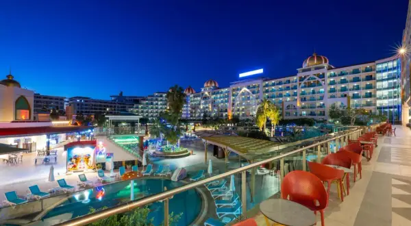 Abendansicht des Alan Xafira Deluxe Resort & Spa mit beleuchteten Pools, Palmen und stilvollen roten Stühlen auf der Terrasse.