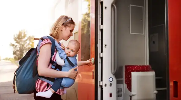 Frau mit Baby im Tragetuch steigt in den Zug. Abenteuerliches Backpacking mit Baby beginnt.