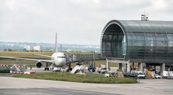 Flugzeug am Gate mit modernem Terminalgebäude. Die Frage "paris welcher flughafen am besten" wird hier nicht beantwortet, aber die Szene zeigt einen belebten Flughafen.