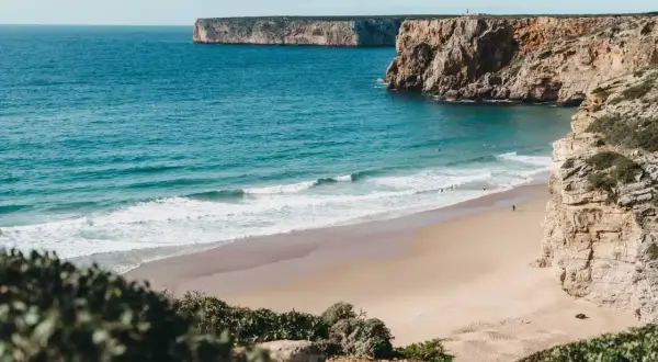 Traumhafter Strand mit Klippen und türkisfarbenem Meer. Perfekt für einen Portugal Urlaub mit Surfern im Wasser.