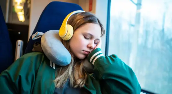 Mädchen schläft im Zug mit gelben Kopfhörern und einem Nackenkissen richtig benutzt für bequemen Halt.