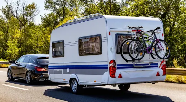 Schwarzer Kombi zieht Wohnwagen mit Fahrrädern, bereit für den Urlaub. B96 oder BE, das ist hier die Frage für die Reise.