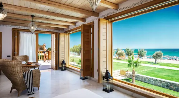 Ein luxuriöses Zimmer mit Meerblick im Mitsis Blue Domes. Eine Frau steht auf dem Balkon und genießt die Aussicht.