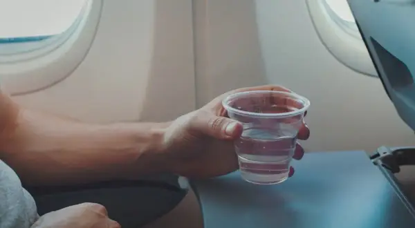 Hand hält ein Glas Wasser, während man im Flugzeug sitzt.