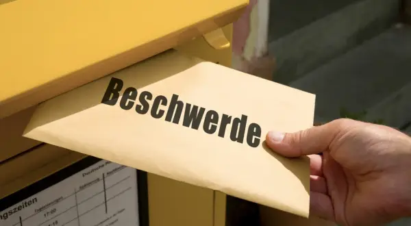 Ein Brief mit der Aufschrift "Beschwerde" wird in einen gelben Briefkasten eingeworfen. Vielleicht eine TUI Reklamation?