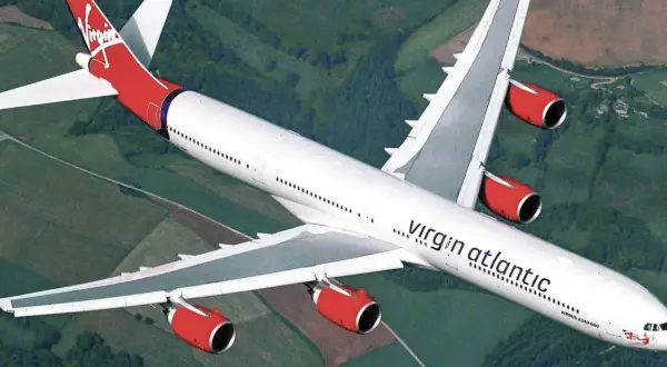 Ein Airbus A340-600 der Virgin Atlantic Flotte fliegt über grüne Landschaften.