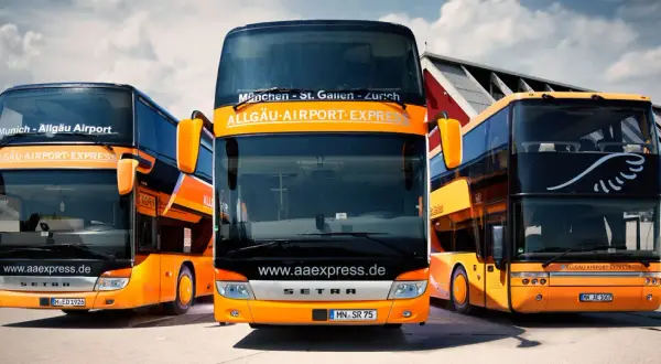Drei orange-schwarze Doppeldeckerbusse von Allgäu Airport Express stehen bereit. Informieren Sie sich über die alex airport shuttle preise für Ihre Reise.