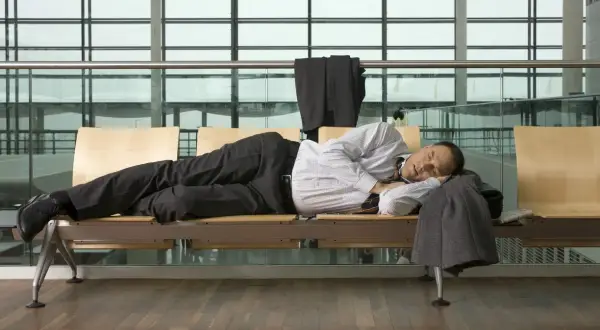 Mann schläft am flughafen auf einer Bank, sein Anzug hängt über der Lehne.