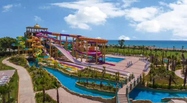 Ein riesiger Wasserpark mit bunten Rutschen, einem Lazy River und Pools. Das Meer im Hintergrund. Ein delphin be grand Urlaubstraum.