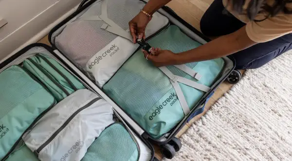 Frauen packen ihre Koffer mit praktischen Reise-Must-Haves: Packwürfel in Mintgrün und Grau sortieren Kleidung für die nächste Reise.