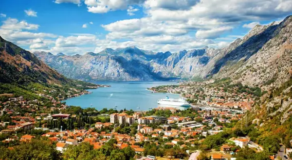 Traumhafter Urlaub in Montenegro: Die Bucht von Kotor mit Kreuzfahrtschiff und malerischer Stadt vor imposanter Bergkulisse.