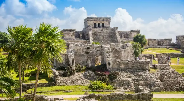 Ruinen von Tulum, ein Traumziel für jeden Mexiko Urlaub. Palmen und antike Bauten unter blauem Himmel.